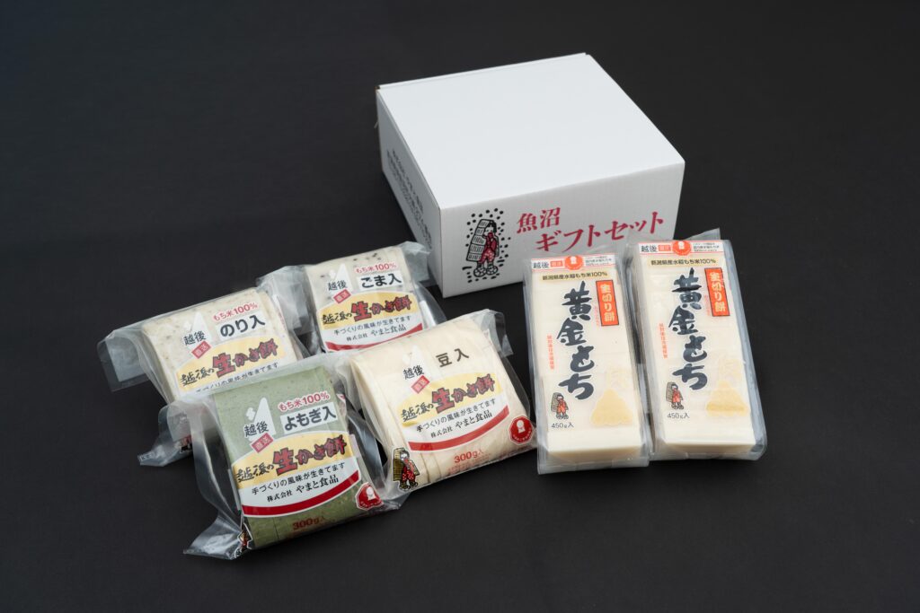 黒い背景に映える、やまと食品の「黄金もち」と「草もち」のパッケージ。魚沼ギフトセットの白い箱を背面に配した、高級感のある構成。