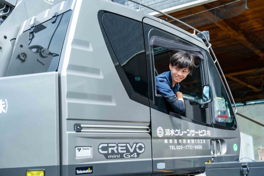 タダノ製クレーン「CREVO mini G4」の運転席から顔を出し、爽やかな笑顔を見せる若手社員。