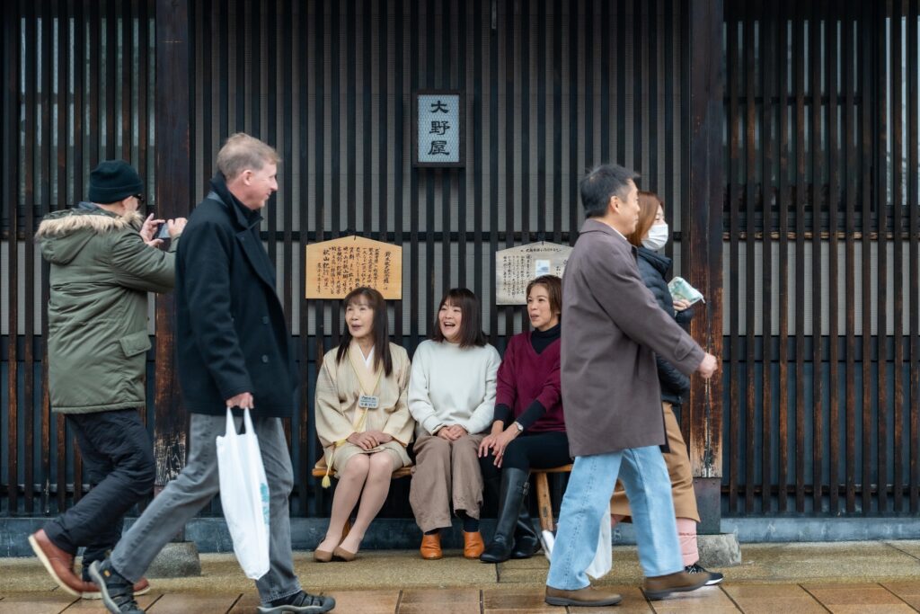 牧之通りの老舗「大野屋」前のベンチに座り、街の賑わいの中で笑顔を見せるガイドグループ雪彩のメンバー。