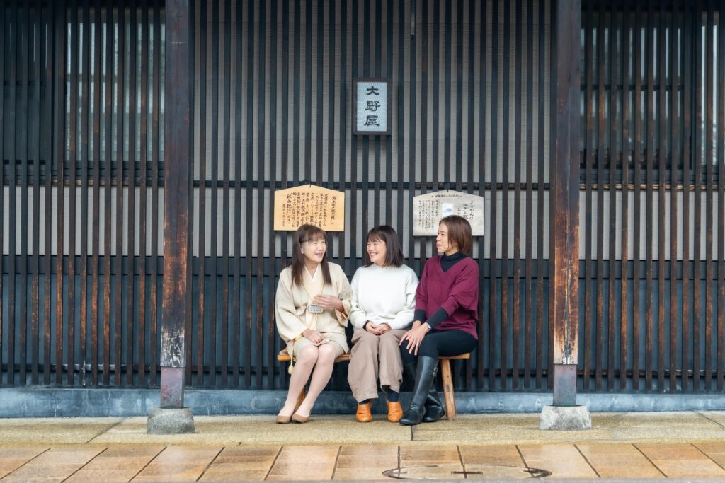 牧之通りの老舗「大野屋」前のベンチに座り、街の賑わいの中で笑顔を見せるガイドグループ雪彩のメンバー。
