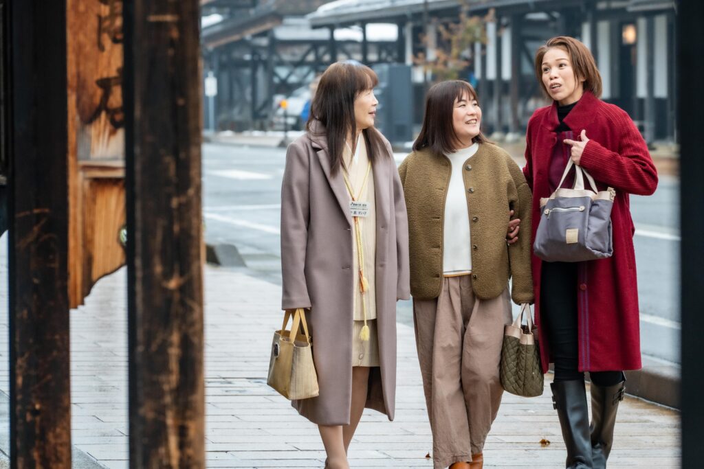 雪国の風情が残る牧之通りを、笑顔で談笑しながら歩くガイドグループ雪彩の3人のメンバー。